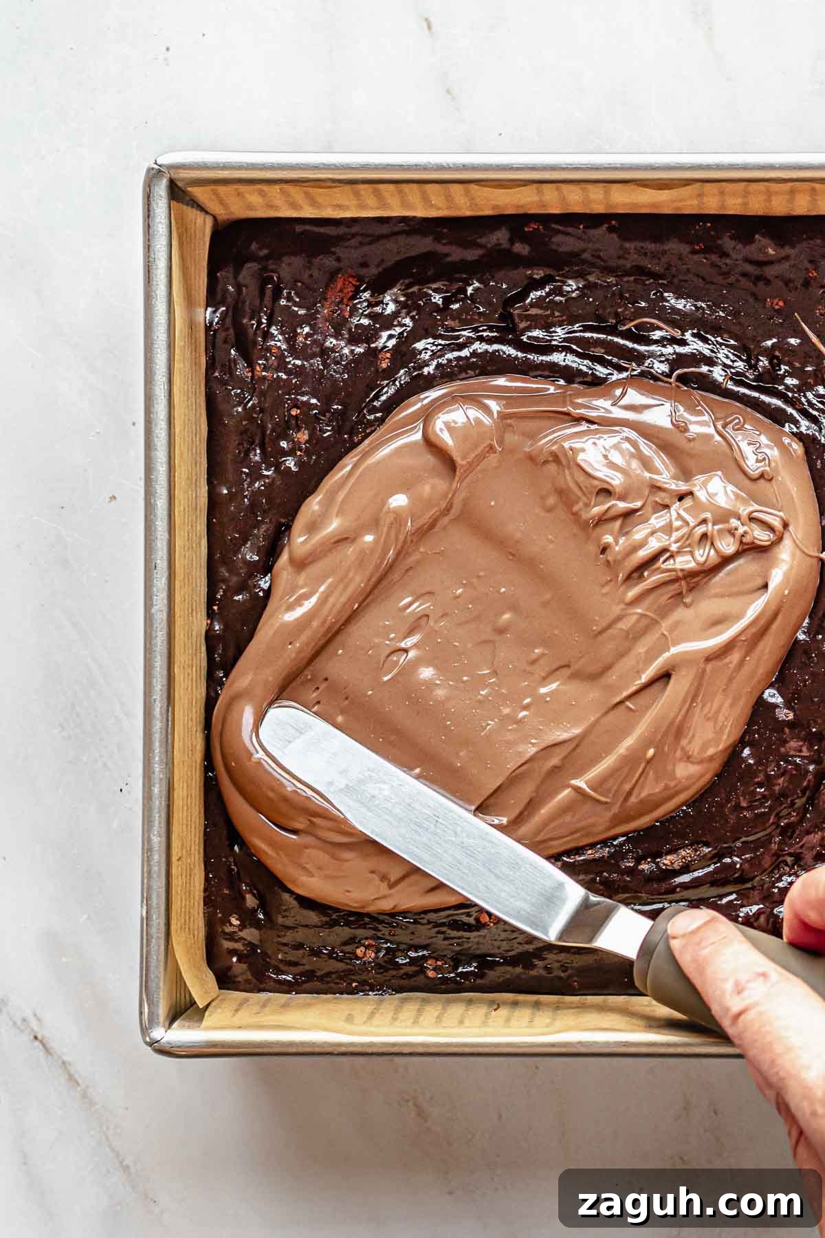 Ferrero Rocher Chocolate Brownies Recipe: Decadent Hazelnut Treat 13 A spatula spreads Nutella on top of brownie batter.