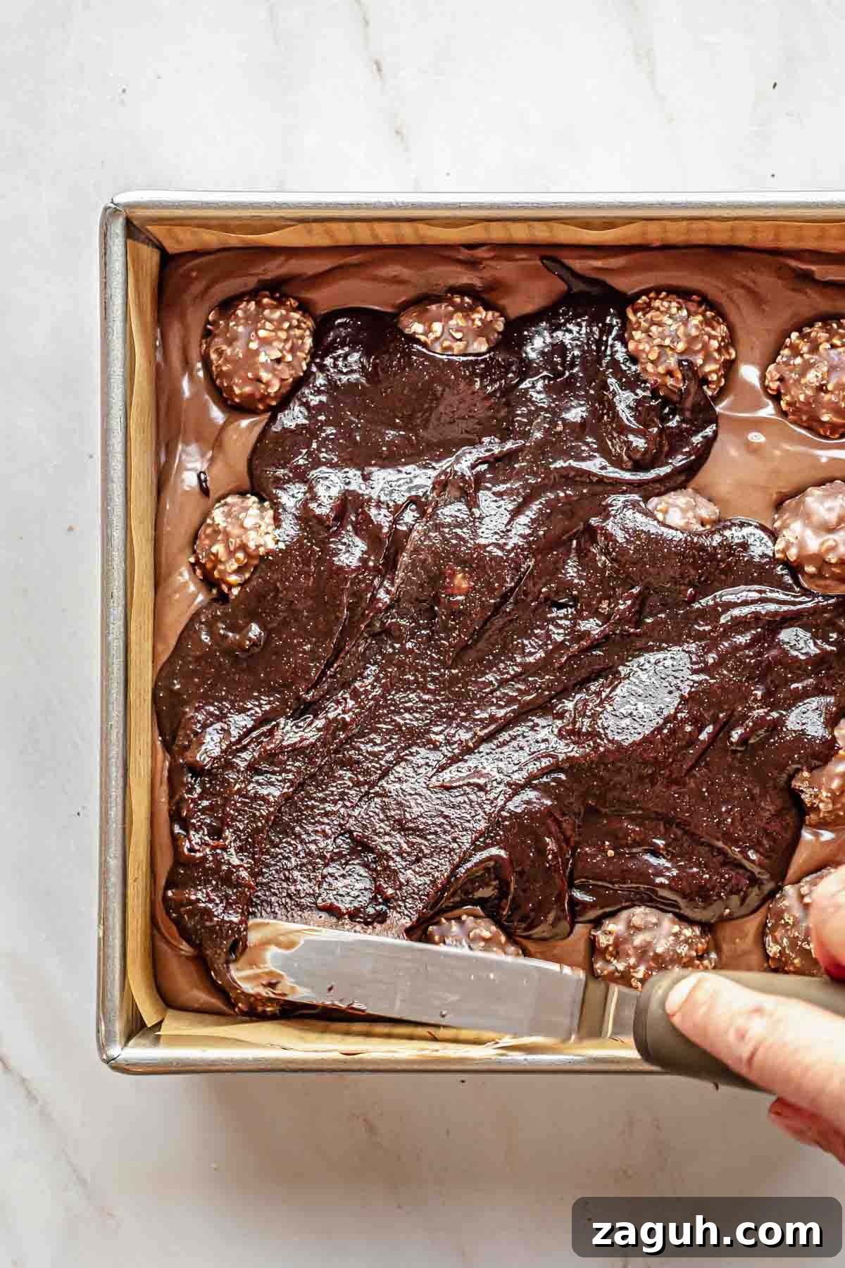 Ferrero Rocher Chocolate Brownies Recipe: Decadent Hazelnut Treat 15 A spatula spreads brownie batter over the Ferrero rocher.