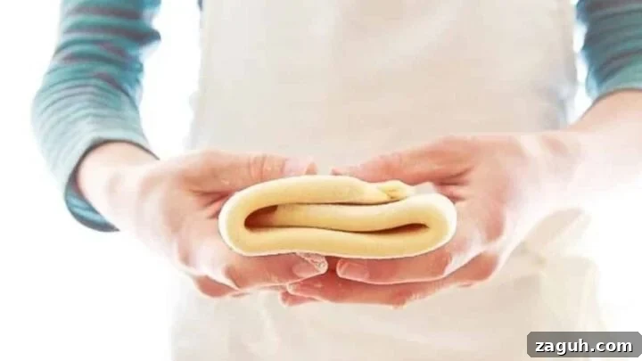 Woman in blue shirt and white apron holding folded puff pastry recipe.