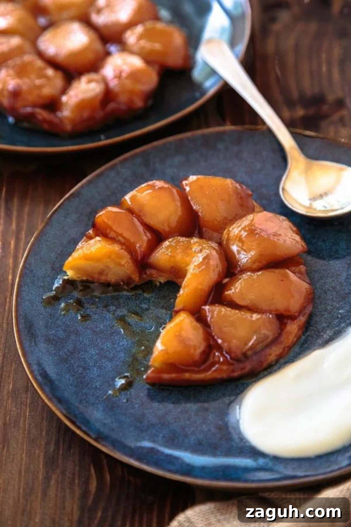 Perfect Puff Pastry Dough: Step-by-Step Homemade Recipe 7 Two servings of apple tarte tatin on dark blue plates with cream dollop.